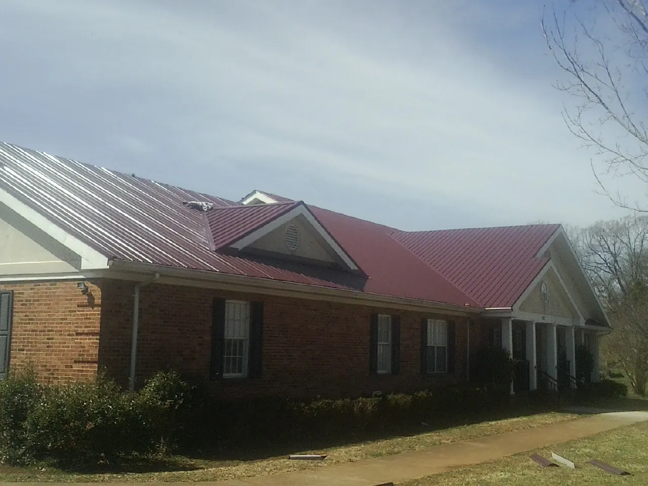 Red metal roof with gabled entries on a long brick building, from a Hail Damage Roof Repair job in Kingsville