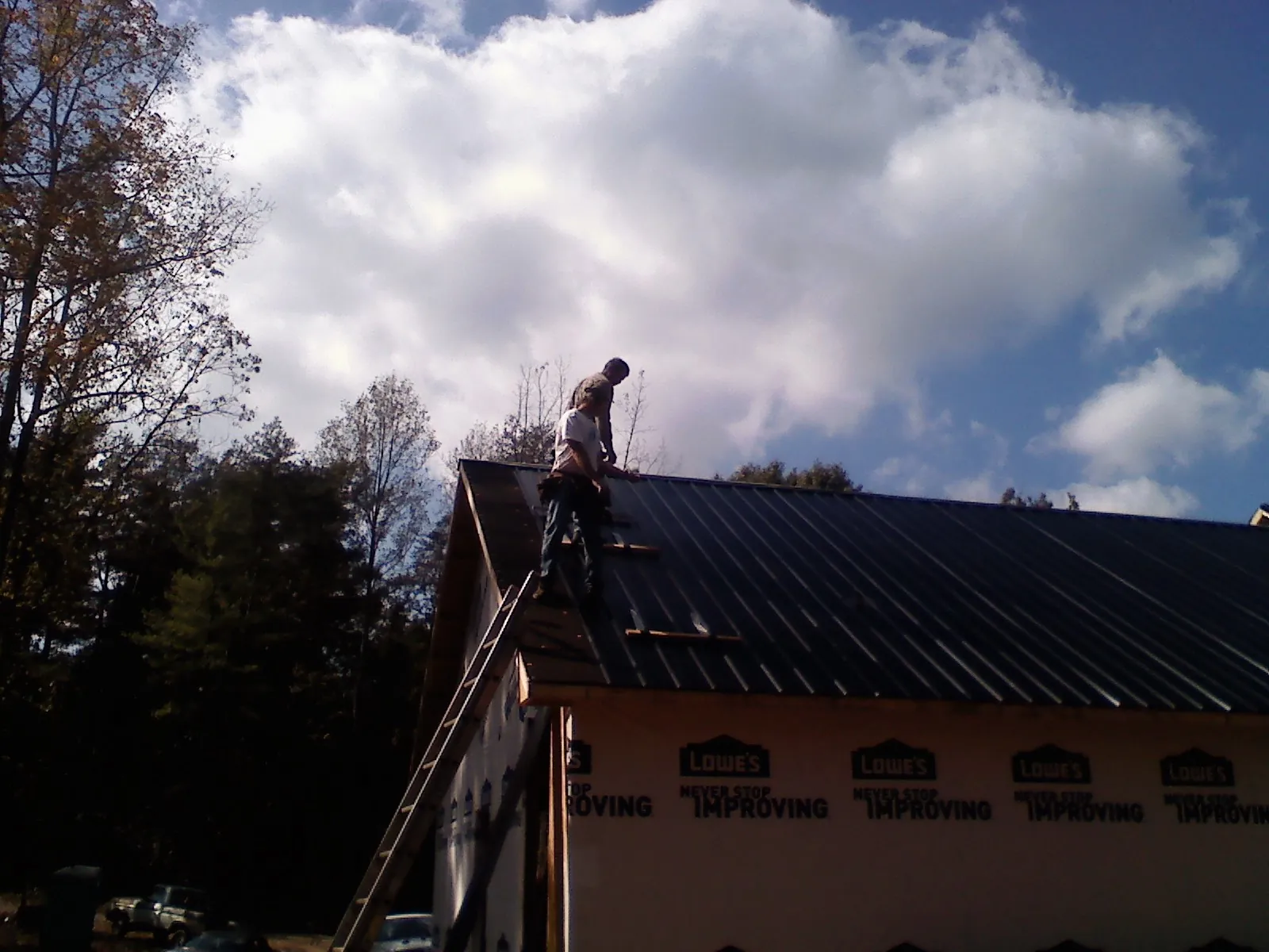 Roofer fastening dark metal panels high against a cloudy sky, from a Roof Inspection job in Kingsville