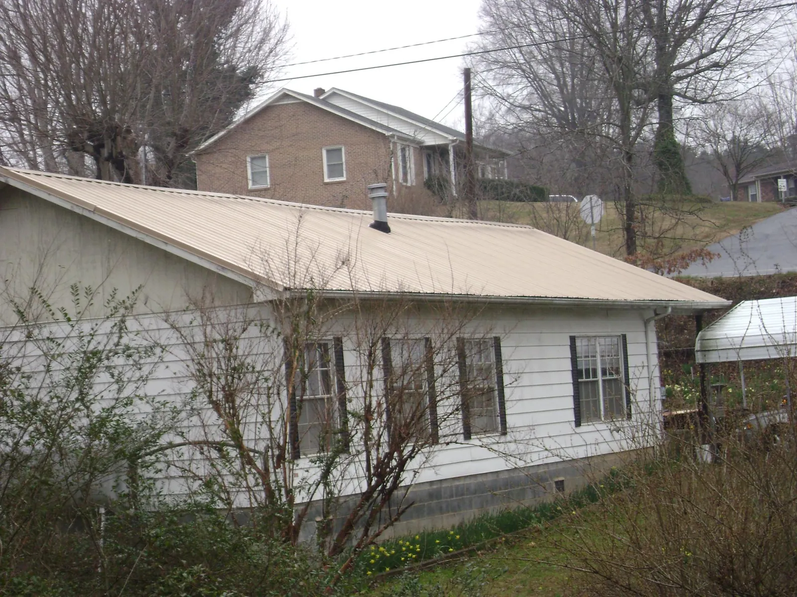 Tan metal roof on a white sided house set into a hillside — Commercial Roofing by Roofing Brothers in Kingsville